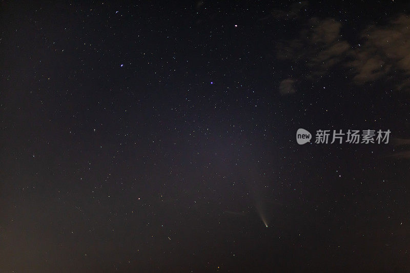 Comet NEOWISE on a dark starry sky with clouds next to the Ursa Major above the horizon at night. Horizontal orientation